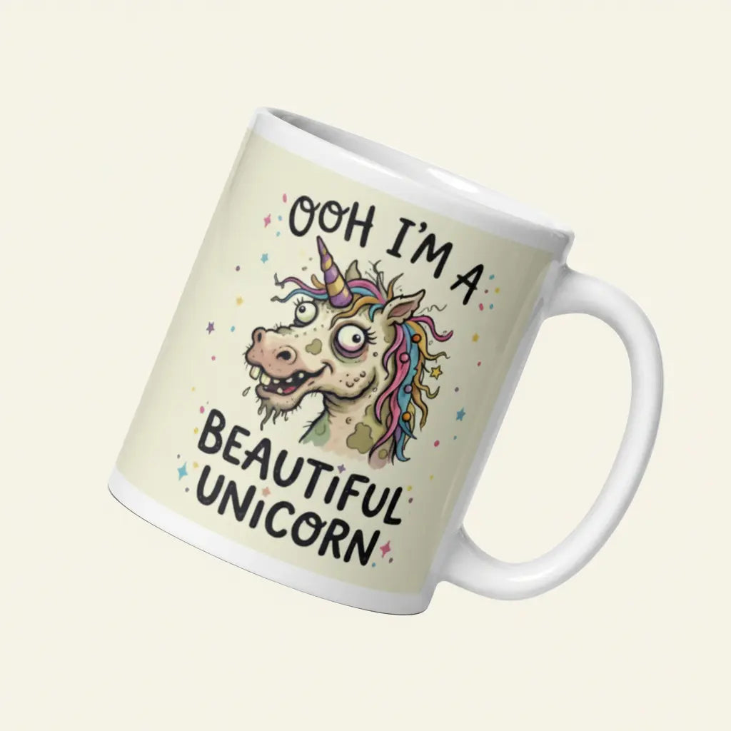 A funny, chaotic illustration on a white ceramic mug of a deranged, ugly unicorn with bloodshot eyes, crooked teeth, and messy pastel hair. The text reads OOH I'M A BEAUTIFUL UNICORN surrounded by small stars.