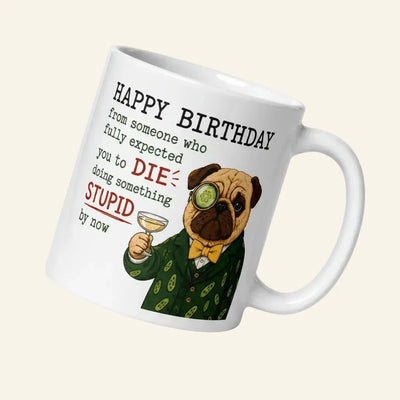 A funny graphic on a transparent background featuring Sir Cucumber Dog, a pug in a green suit and monocle, raising a champagne glass. Text reads: HAPPY BIRTHDAY from someone who fully expected you to DIE doing something STUPID by now.