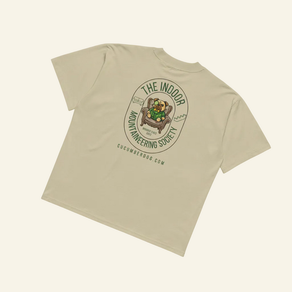 The back of an oversized t-shirt featuring a circular green crest. The text reads The Indoor Mountaineering Society. In the center is a posh pug in a green suit sitting in an armchair, flanked by a drawing of a sofa and stairs.