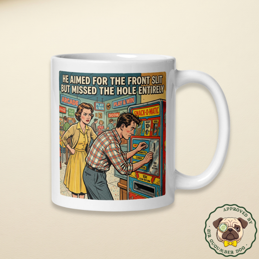 White ceramic coffee mug featuring a sarcastic retro comic of a man failing at an arcade machine with the text He aimed for the front slit but missed the hole entirely, sitting on a wooden kitchen table next to a plush pug dog wearing a green suit, yellow bow tie, and a cucumber monocle.