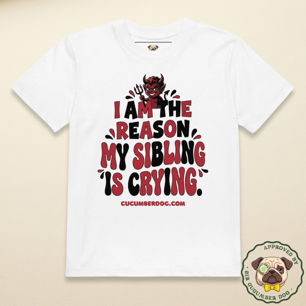 A white organic cotton children's t-shirt featuring a mischievous red cartoon devil holding a pitchfork above bold typography that reads: I AM THE REASON MY SIBLING IS CRYING.