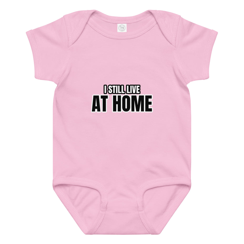 Pink baby onesie with 'I STILL LIVE AT HOME' text on a white background. Cucumber Dog