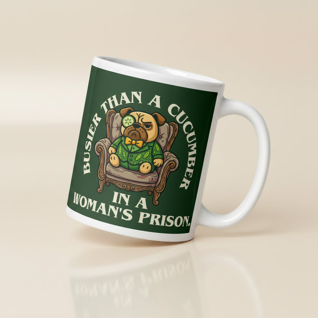 A tilted white ceramic mug with a large dark green label. In the centre of the label, a pug named Sir Cucumber Dog sits in an armchair wearing a cucumber suit and monocle. The white text reads BUSIER THAN A CUCUMBER IN A WOMAN S PRISON.