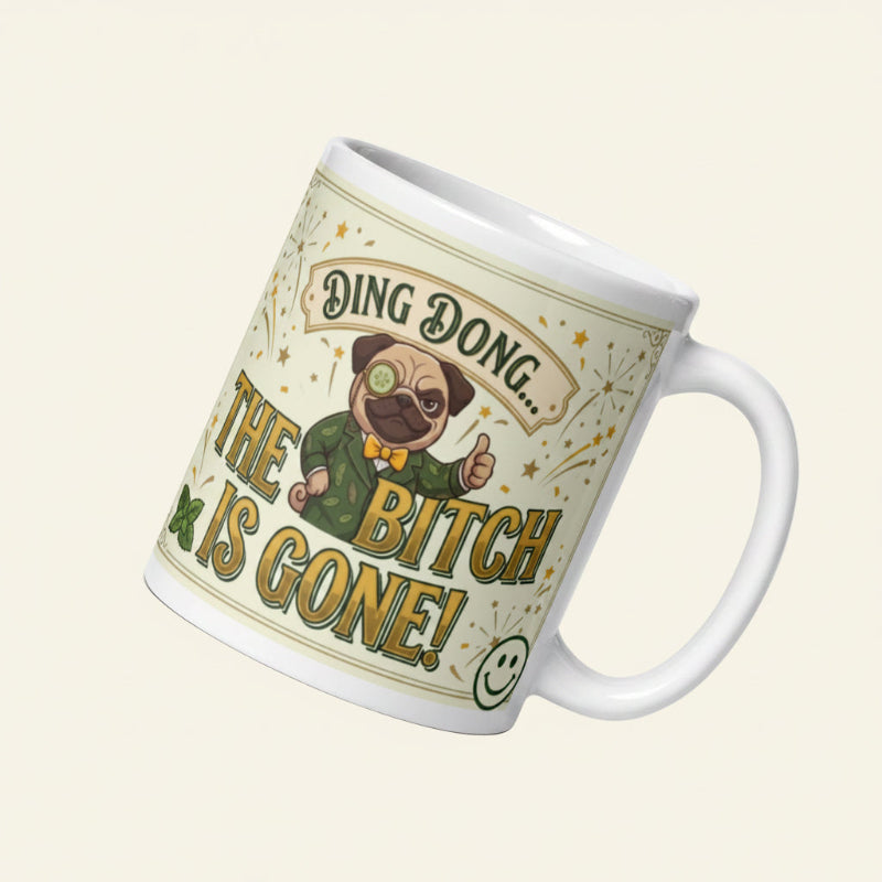 A funny, vintage-inspired graphic on a light cream background with a gold border. Features a pug named Sir Cucumber Dog wearing a monocle and a green suit, giving a thumbs up next to the bold text DING DONG... THE BITCH IS GONE! surrounded by illustrated fireworks. 11 oz