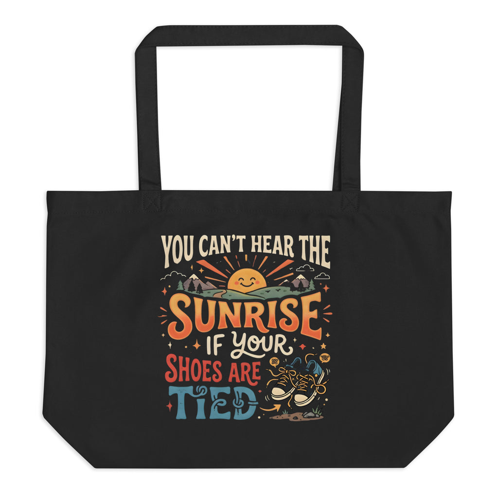 A large black eco tote bag featuring a retro 1970s design of a smiling sun and mountains with the funny, nonsensical quote You Can Not Hear The Sunrise If Your Shoes Are Tied.