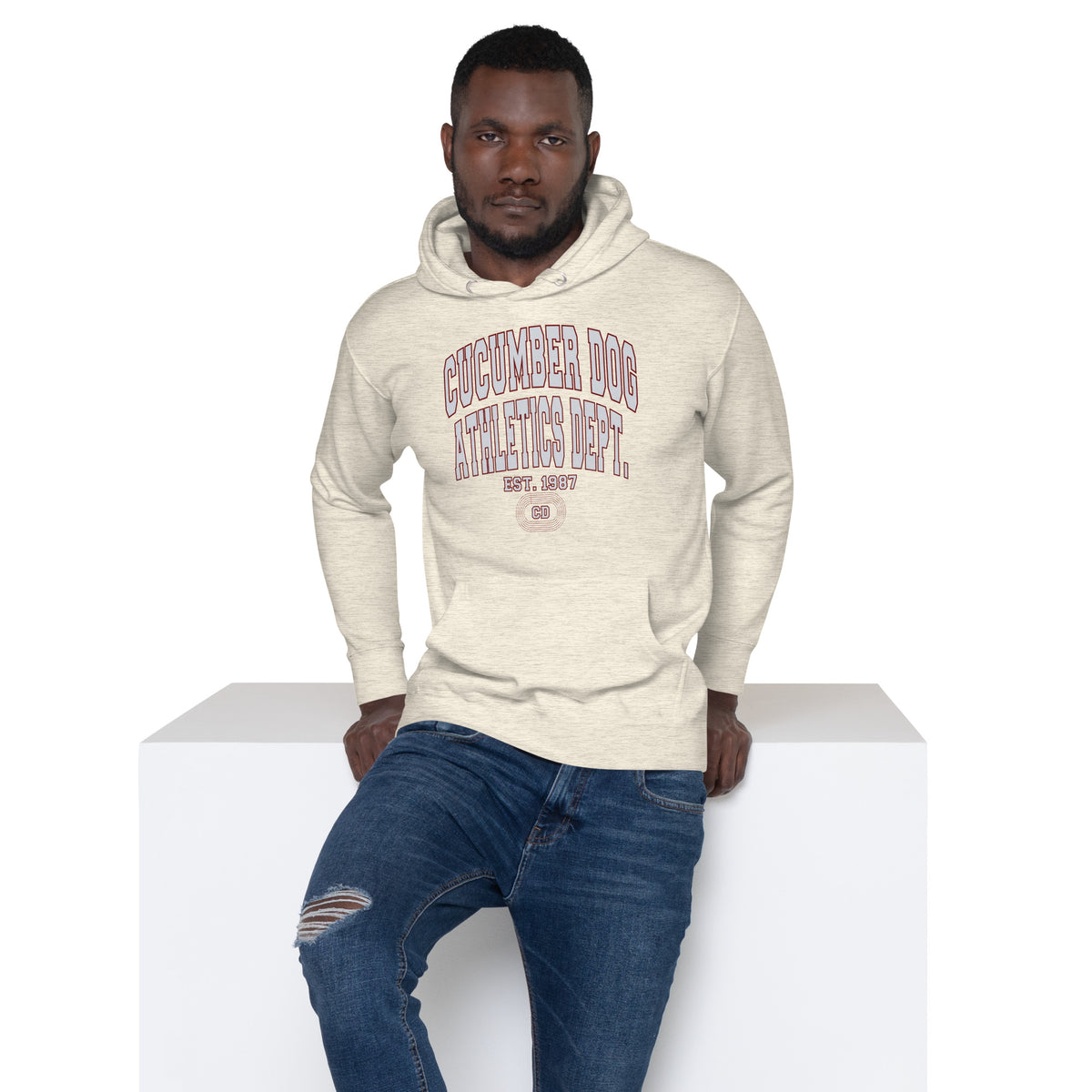 Premium oatmeal heather hoodie featuring a vintage athletic graphic with arched Cucumber Dog and Athletics Dept text in grey block typography with a maroon outline, above Est. 1987 and a track motif framing the CD monogram.