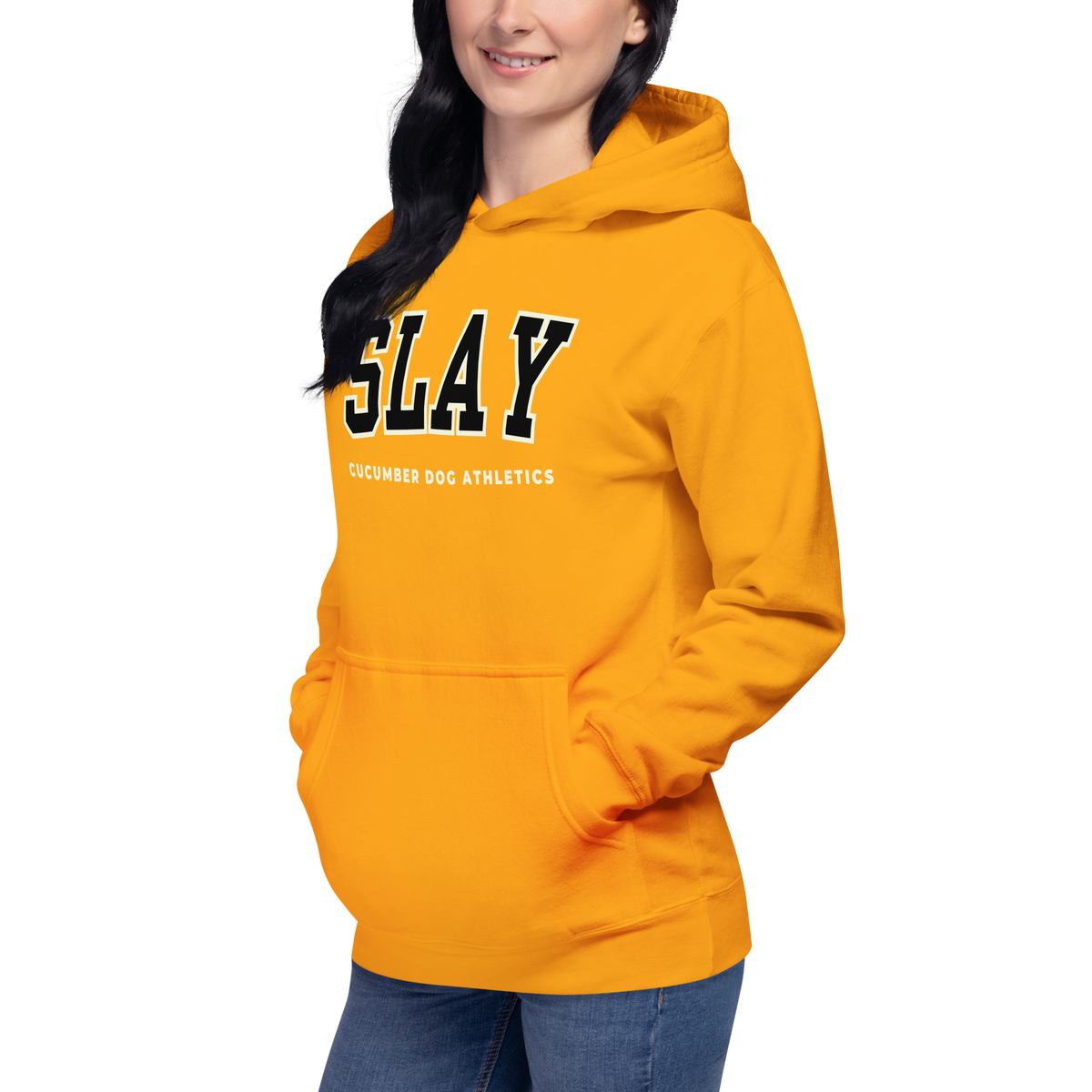 A woman wearing a bright gold pullover hoodie with 'SLAY' and 'CUCUMBER DOG ATHLETICS' printed on the front, paired with blue jeans, against a plain white background.