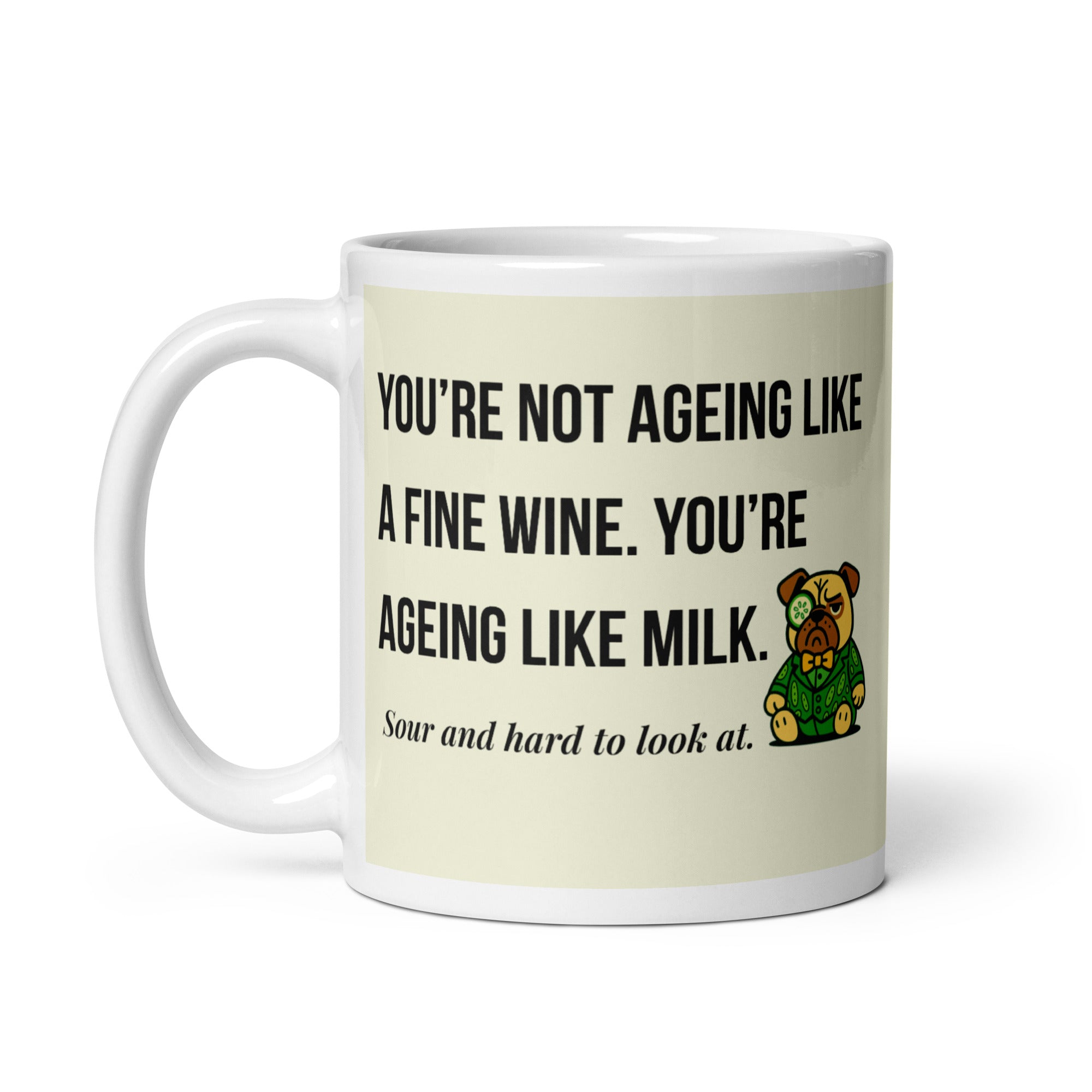 White glossy mug featuring Sir Cucumber Dog the pug. The text "YOU'RE NOT AGEING LIKE A FINE WINE. YOU'RE AGEING LIKE MILK. SOUR AND HARD TO LOOK AT." is rendered in Cucumber green over a vibrant cream background banner.