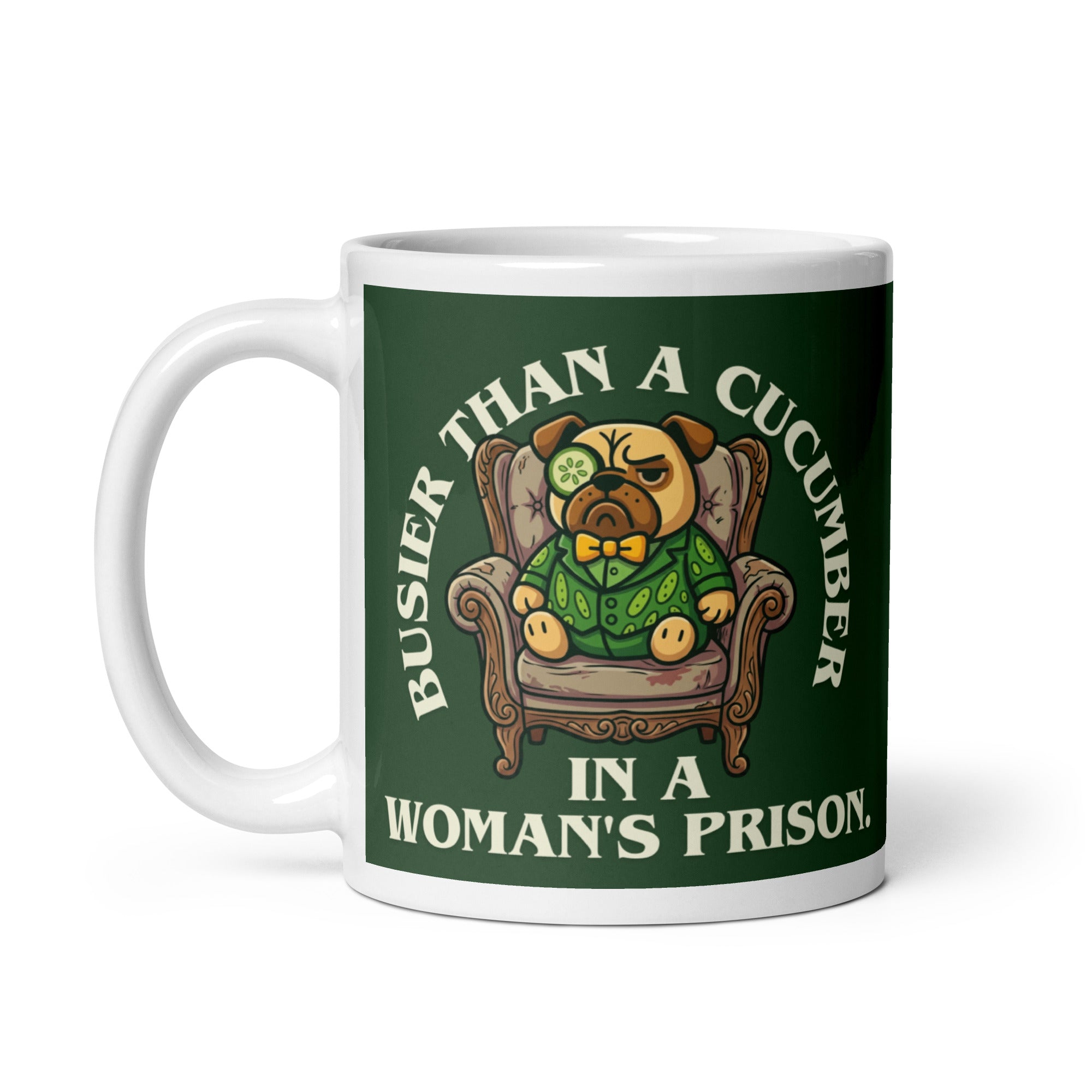 A tilted white ceramic mug with a large dark green label. In the centre of the label, a pug named Sir Cucumber Dog sits in an armchair wearing a cucumber suit and monocle. The white text reads BUSIER THAN A CUCUMBER IN A WOMAN S PRISON.