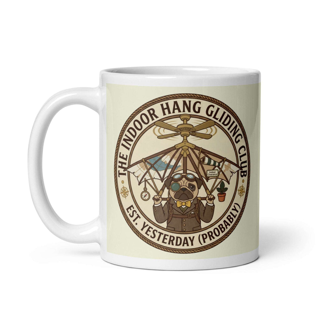A circular vintage emblem on a transparent background. It reads THE INDOOR HANG GLIDING CLUB EST. YESTERDAY (PROBABLY). Inside, Sir Cucumber Dog wears a tweed suit and aviator goggles, strapped to a hang glider that is attached to a ceiling fan. 11 oz