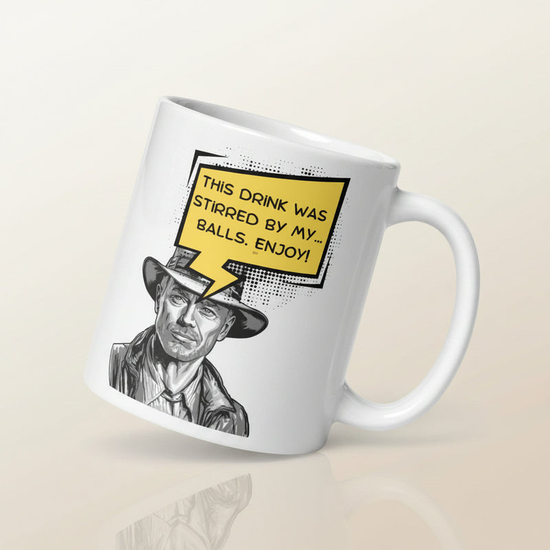 White glossy mug featuring a grayscale sketch of a rugged adventurer and a yellow speech bubble saying: This drink was stirred by my balls. Enjoy!