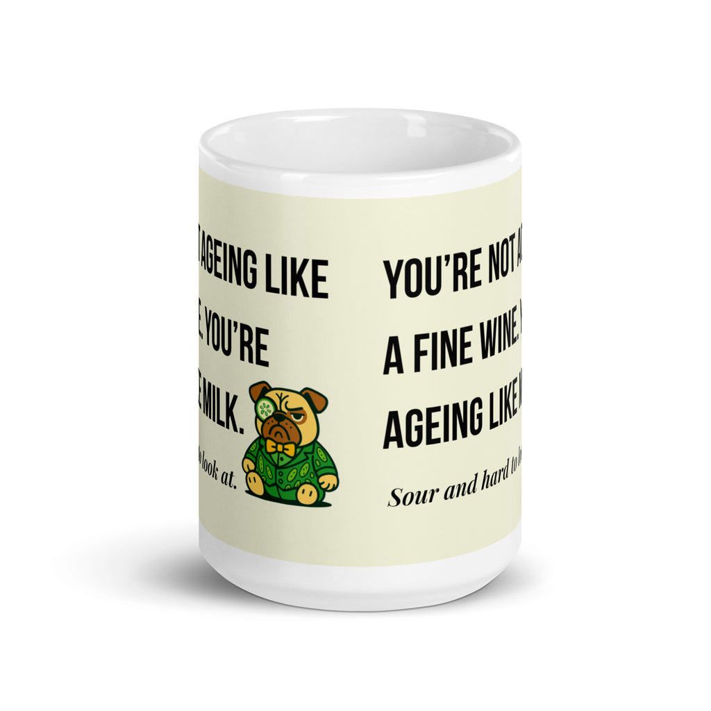 White glossy mug featuring Sir Cucumber Dog the pug. The text "YOU'RE NOT AGEING LIKE A FINE WINE. YOU'RE AGEING LIKE MILK. SOUR AND HARD TO LOOK AT." is rendered in Cucumber green over a vibrant cream background banner. 15oz