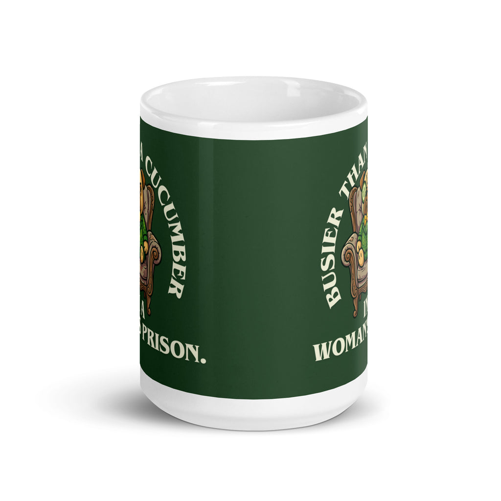 A tilted white ceramic mug with a large dark green label. In the centre of the label, a pug named Sir Cucumber Dog sits in an armchair wearing a cucumber suit and monocle. The white text reads BUSIER THAN A CUCUMBER IN A WOMAN S PRISON. 15oz
