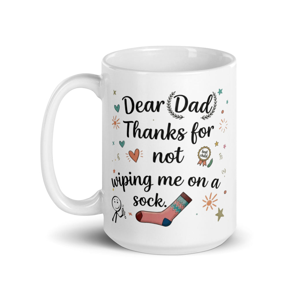A white ceramic mug on a white surface. The design features playful, hand drawn style text that reads DEAR DAD THANKS FOR NOT WIPING ME ON A SOCK. The typography is surrounded by whimsical icons including a pink patterned sock, a smiling stick figure, a gold best child medal, and small sun and heart illustrations. 15oz