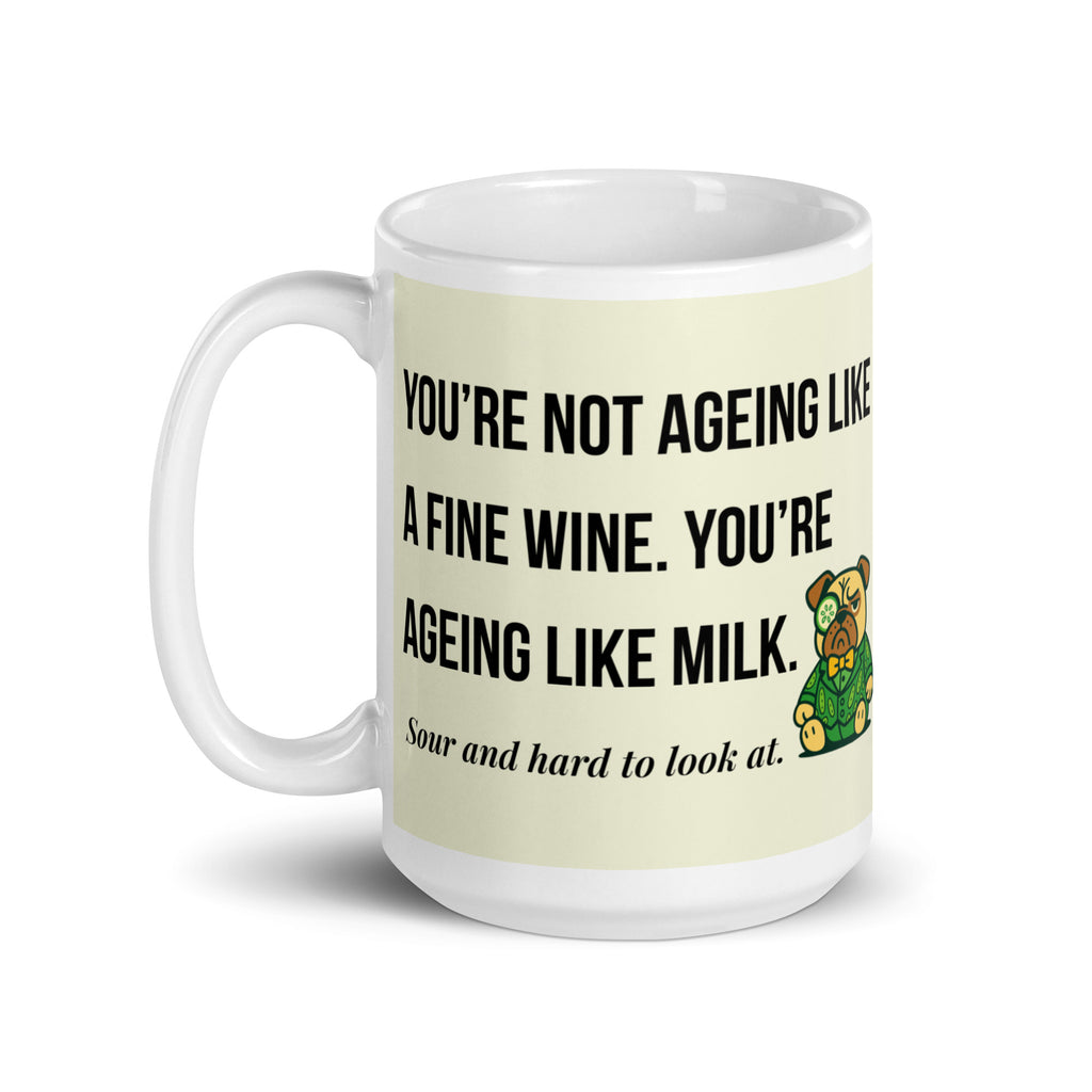 White glossy mug featuring Sir Cucumber Dog the pug. The text "YOU'RE NOT AGEING LIKE A FINE WINE. YOU'RE AGEING LIKE MILK. SOUR AND HARD TO LOOK AT." is rendered in Cucumber green over a vibrant cream background banner. 15oz
