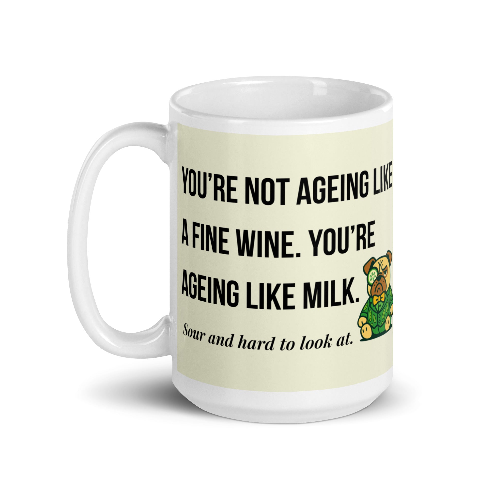 White glossy mug featuring Sir Cucumber Dog the pug. The text "YOU'RE NOT AGEING LIKE A FINE WINE. YOU'RE AGEING LIKE MILK. SOUR AND HARD TO LOOK AT." is rendered in Cucumber green over a vibrant cream background banner. 15oz